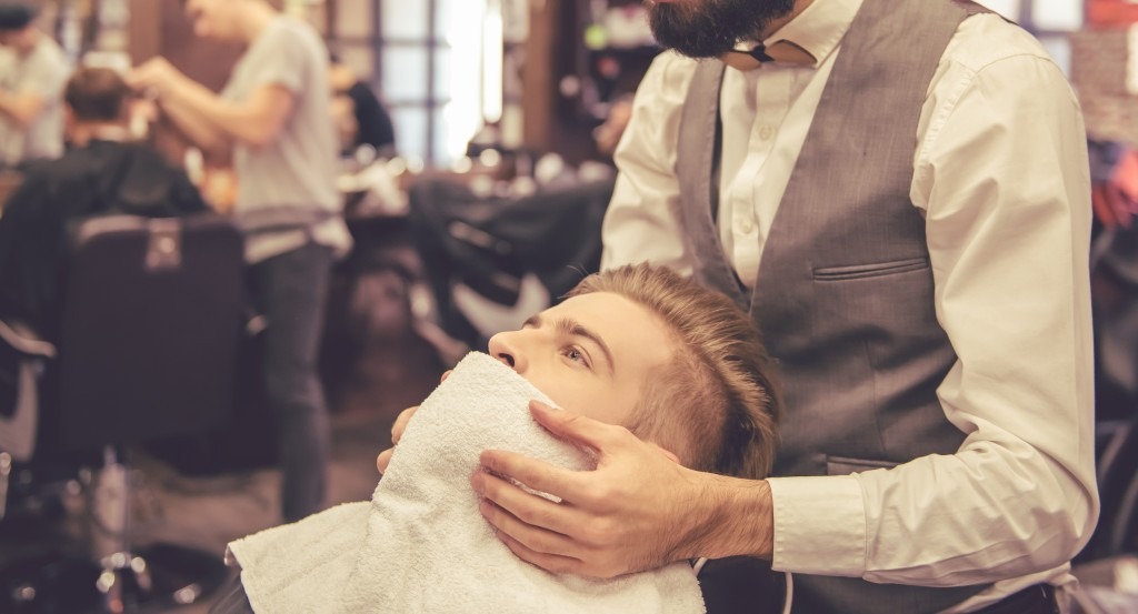 Brodaty mężczyzna stylizowany przez barbera w barbershopie (źródło Envato)